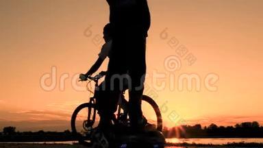 日出时青少年的剪影。 一个男孩骑着一个自平衡的双轮陀螺，另一个年轻人骑着自行车。